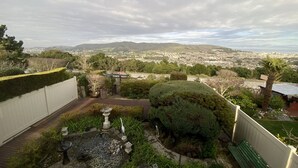 Een tuin met een vijver, een bankje en uitzicht op een stadsgezicht met bergen in de verte.