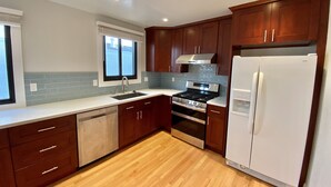 Een moderne keuken met houten kastjes, een roestvrijstalen fornuis, een witte koelkast en een raam met jaloezieën.