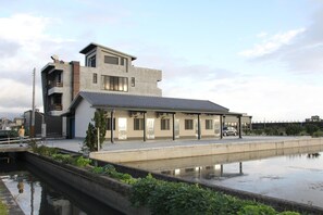 A modern building with a flat roof, a covered walkway, and a water feature in front. - Howj Hostel (Zhuangwei)