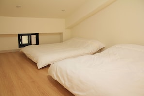 A bedroom with two single beds, wooden flooring, and a small window with a mirror. - Howj Hostel (Zhuangwei)