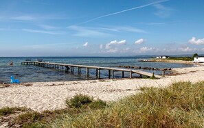 A beach with a wooden pier extending into the water, a sandy shore, and a small building in the background. - Amazing home in Ebeltoft with WiFi (Ebeltoft)