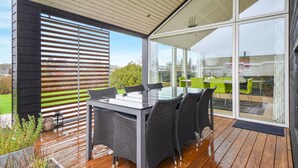 Un espace extérieur aménagé pour les repas, avec une table et des chaises en verre, une terrasse en bois et une vue sur le paysage environnant.