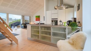 Une cuisine moderne dotée d’un îlot central, d’appareils électroménagers intégrés et d’une grande fenêtre offrant une vue sur l’extérieur.