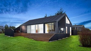 Une maison moderne avec un toit en pente, de grandes fenêtres et une terrasse en bois.