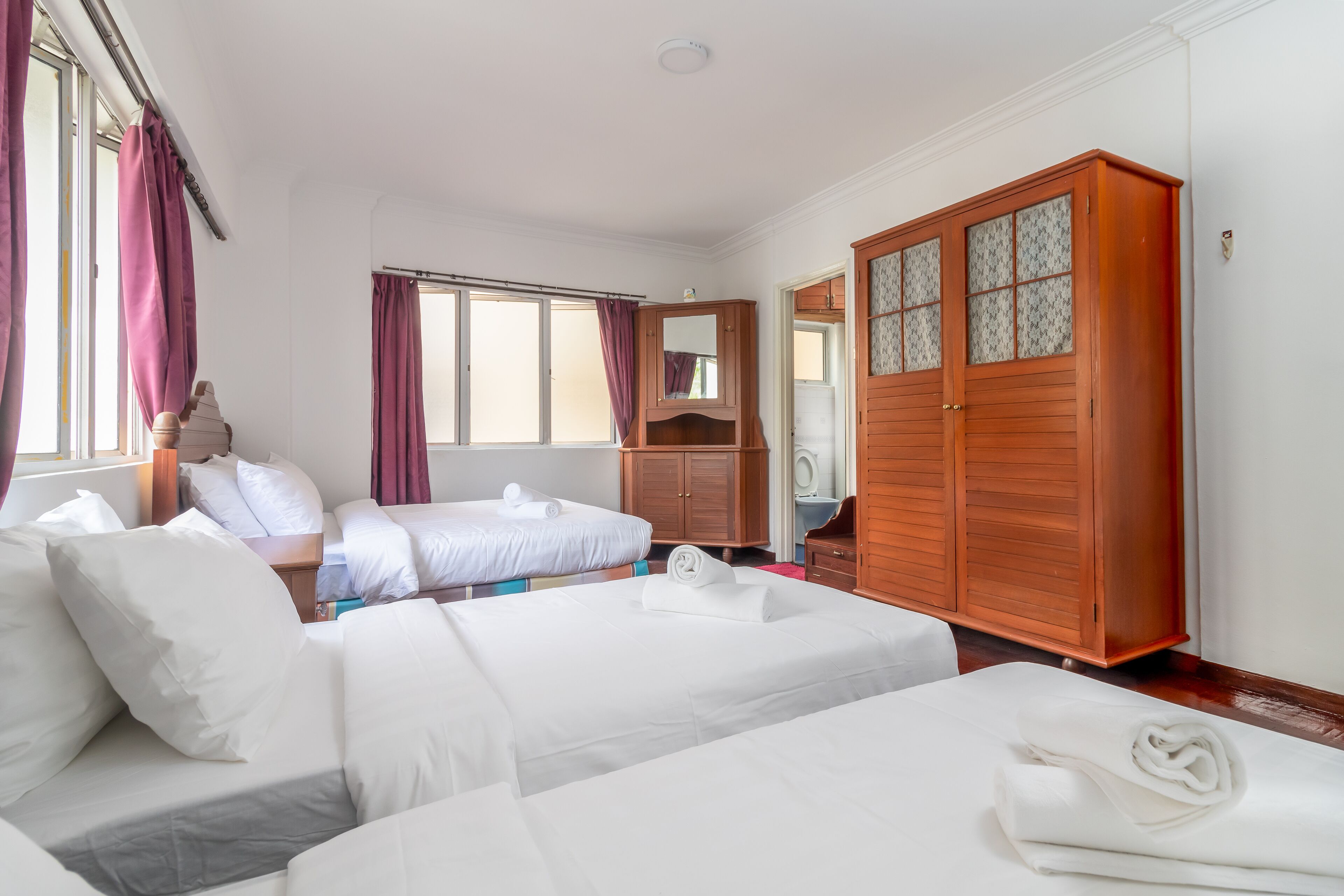 A hotel room with two beds, a wooden wardrobe, a mirror, and a window with curtains.