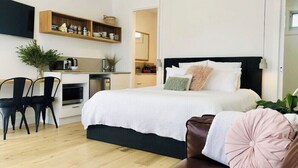 A modern bedroom with a large bed, a desk with a chair, and a kitchenette. - Hakea King Suite- Inlet Waters Escape. Stroll the inlet & nature boardwalk (Inverloch)