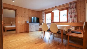 A wooden interior with a dining area, a kitchen with a TV, and a bed in a separate room. - moderne Ferienwohnung/Dalaas (Dalaas)
