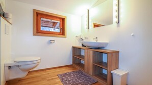 A bathroom with a toilet, a wooden vanity with a vessel sink, a mirror with lights, a window, and a wooden floor. - moderne Ferienwohnung/Dalaas (Dalaas)