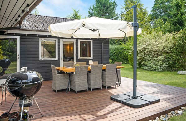 Une terrasse dotée de mobilier d’extérieur, d’un barbecue et d’une pergola surmontée d’un auvent blanc.