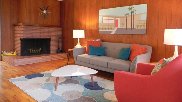 A living room with a fireplace, a sofa, a coffee table, and a painting on the wall. - Mid-Century Modern w/ Garage Close to Amenities & 3 Miles to Autzen/UO! (Eugene)