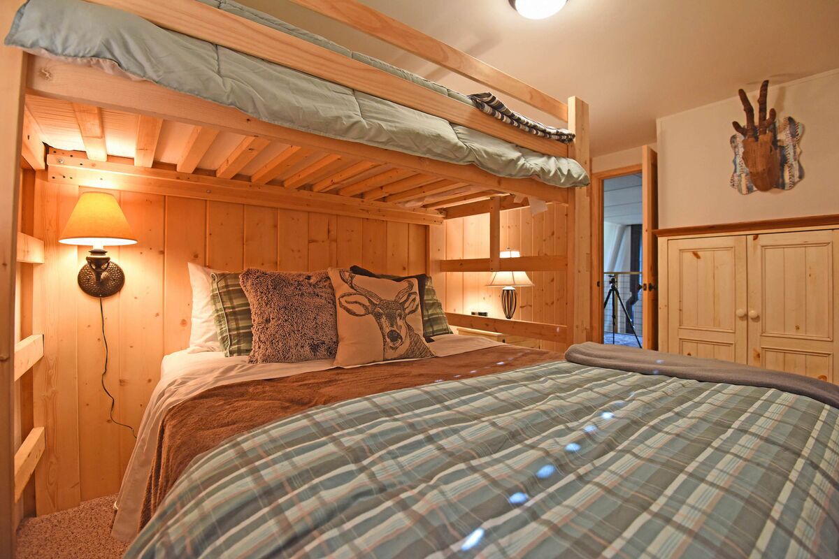 Een knus slaapkamer in een houten hut met een stapelbed, ruitjes beddengoed en een opgehangen dierenhoofd aan de muur.