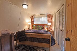 A bedroom with a wooden bed, a bedside table with a lamp, a window with checkered curtains, and a door with a wooden panel. - Tahoe Park Amenities Elevated Mountain Cabin, Beach, Piers and more (Tahoe City)