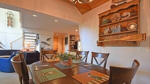 Een eethoek met een ronde tafel, stoelen en placematen. Er is een houten plank met decoratieve borden en een bordje.