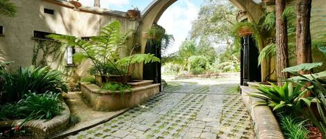 Un patio empedrado con un arco, rodeado de abundante follaje y plantas en macetas.