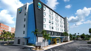 Een modern hotel met een opvallend 'tru' logo, een parkeerplaats en palmbomen.