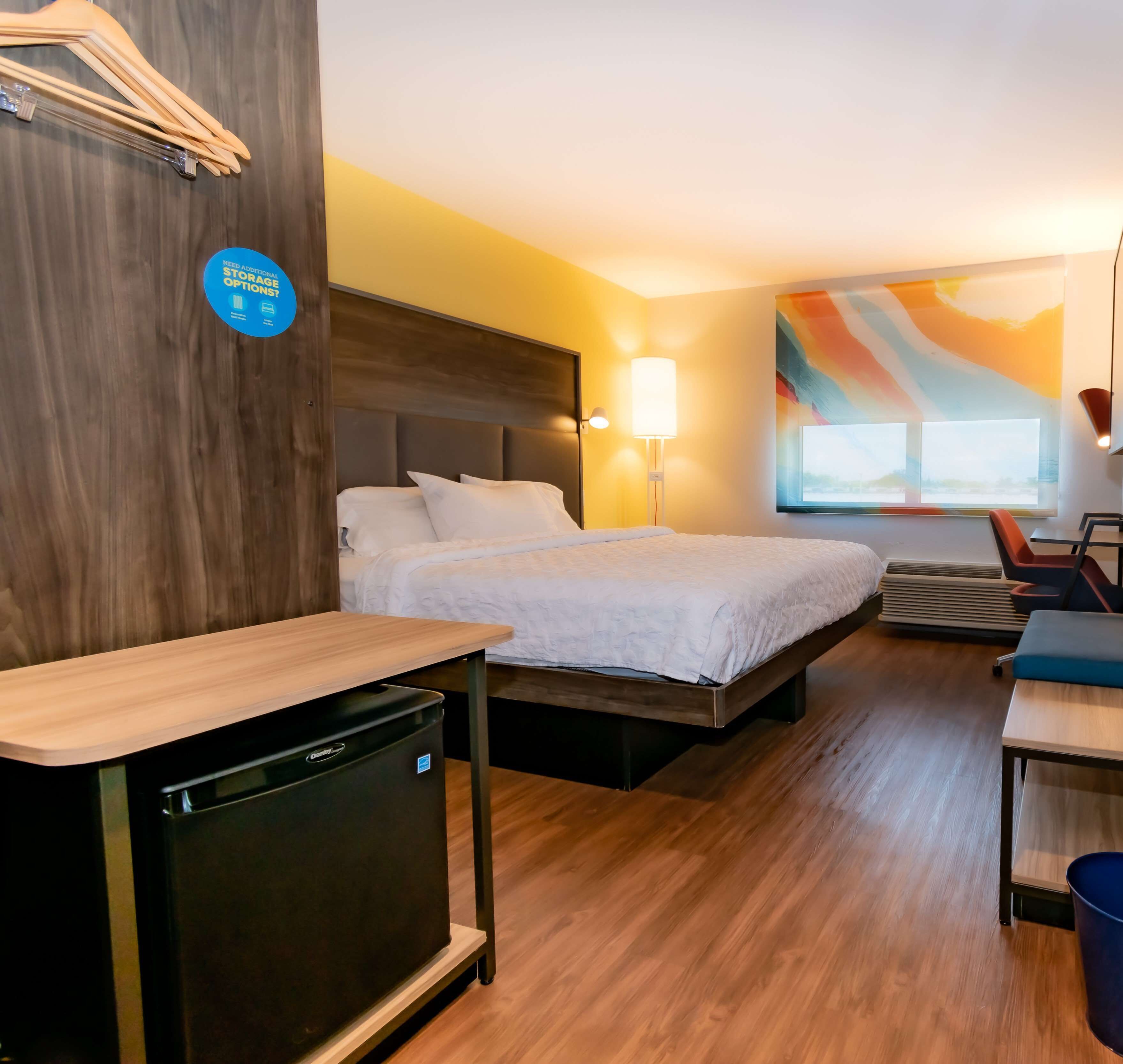 A hotel room with a bed, bedside table, desk, and a wall-mounted lamp.