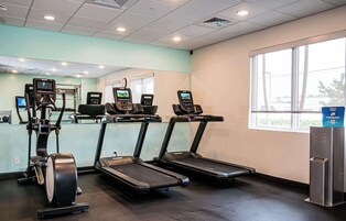 Un gimnasio con cintas de correr, elípticas y una pantalla digital.
