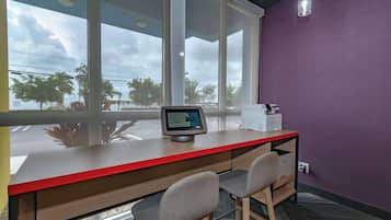 A modern office space with a desk, chairs, a computer monitor, and a window with a view of palm trees and buildings.