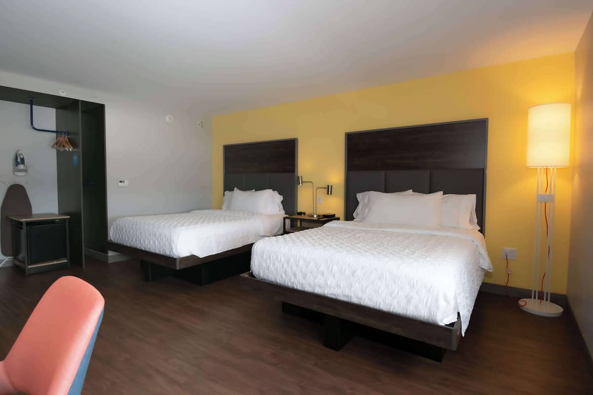 A hotel room with two beds, a desk, a chair, and a floor lamp.