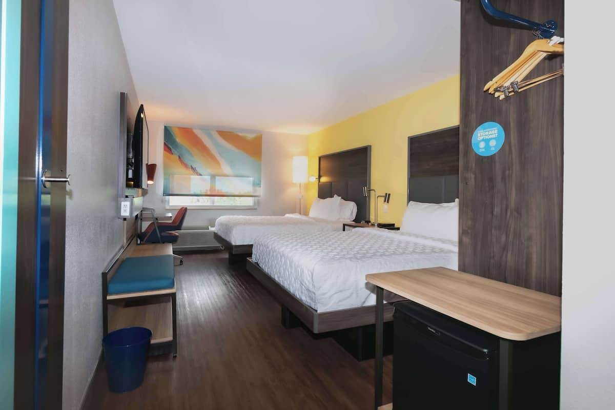 A hotel room with two beds, a desk, a chair, a TV, and a painting on the wall.