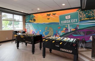 Una habitación con dos mesas de fútbol de mesa, un mural que representa Florida City y vistas al exterior.
