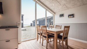 A dining area with a large window overlooking a beach, wooden furniture, and a view of beach houses. - Lovely home in Nyborg (Nyborg)