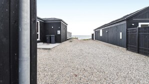 A gravel path leading to a row of dark-colored buildings with a view of the sea. - Lovely home in Nyborg (Nyborg)