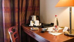 A hotel room with a wooden desk, a lamp, a bottle, a cup, a plate with snacks, a phone, and a notepad. - Hotel Pavillon Monceau by Happy Culture (Paris)