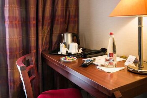 A hotel room with a wooden desk, a lamp, a bottle, a cup, a plate with snacks, a phone, and a notepad. - Hotel Pavillon Monceau by Happy Culture (Paris)