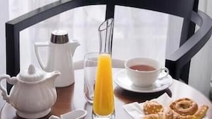 A breakfast table with a pitcher, a glass of orange juice, a cup of tea, and pastries. - Hotel Pavillon Monceau by Happy Culture (Paris)