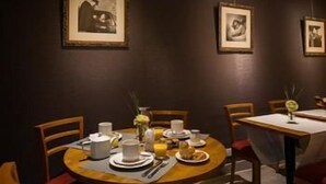 A dining area with round tables, chairs, and framed pictures on the wall. - Hotel Pavillon Monceau by Happy Culture (Paris)