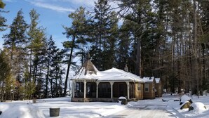A snow-covered wooden cabin with a porch, surrounded by tall pine trees. - BEAUTIFUL FOUR SEASON WATERFRONT COTTAGE (Innisfill)