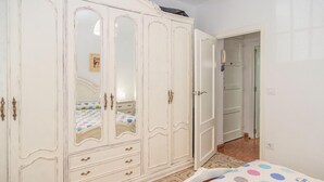 Et soveværelse med en stor, hvid garderobe, en seng med et prikket sengetæppe og et lille natbord.