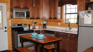 A kitchen with wooden cabinets, a microwave, a stove, a sink, and a refrigerator. - The Ossi is a secluded couples cabin with panoramic mountain and sunset views! (Smithville)