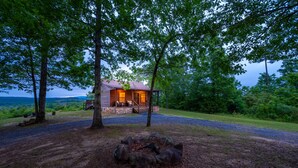 A rustic cabin with a porch, surrounded by trees and a fire pit. - The Ossi is a secluded couples cabin with panoramic mountain and sunset views! (Smithville)