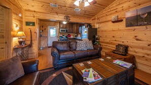 A cozy cabin interior with a leather sofa, a wooden coffee table, and a ceiling fan. - The Ossi is a secluded couples cabin with panoramic mountain and sunset views! (Smithville)