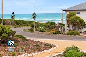 A coastal road with a sandy area and a building with a grey roof.