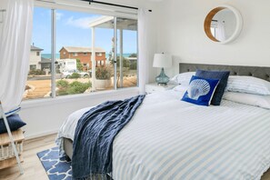A bedroom with a large window, a bed with striped bedding, a round mirror, and a view of the outside.