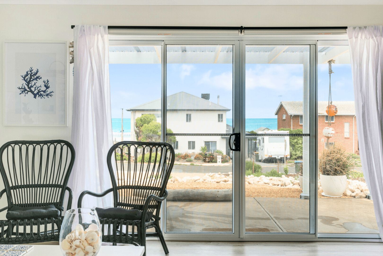 A room with two black chairs, a glass table with a vase, and a sliding glass door leading to an outdoor area with a view of houses and a truck.