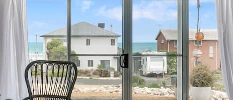 A room with two chairs, a table, and a view of the sea through a sliding glass door.