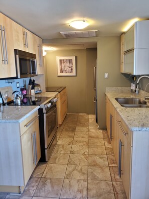A modern kitchen with stainless steel appliances, wooden cabinets, and a tiled floor.