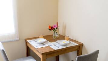 A wooden dining table with two plates, a vase with flowers, and two glasses of orange juice.