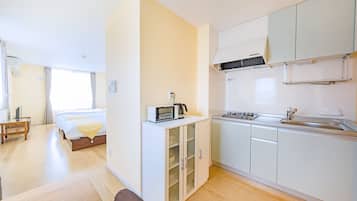 A compact hotel room with a kitchenette, a bed with a yellow bedspread, a small table, and a window with curtains.