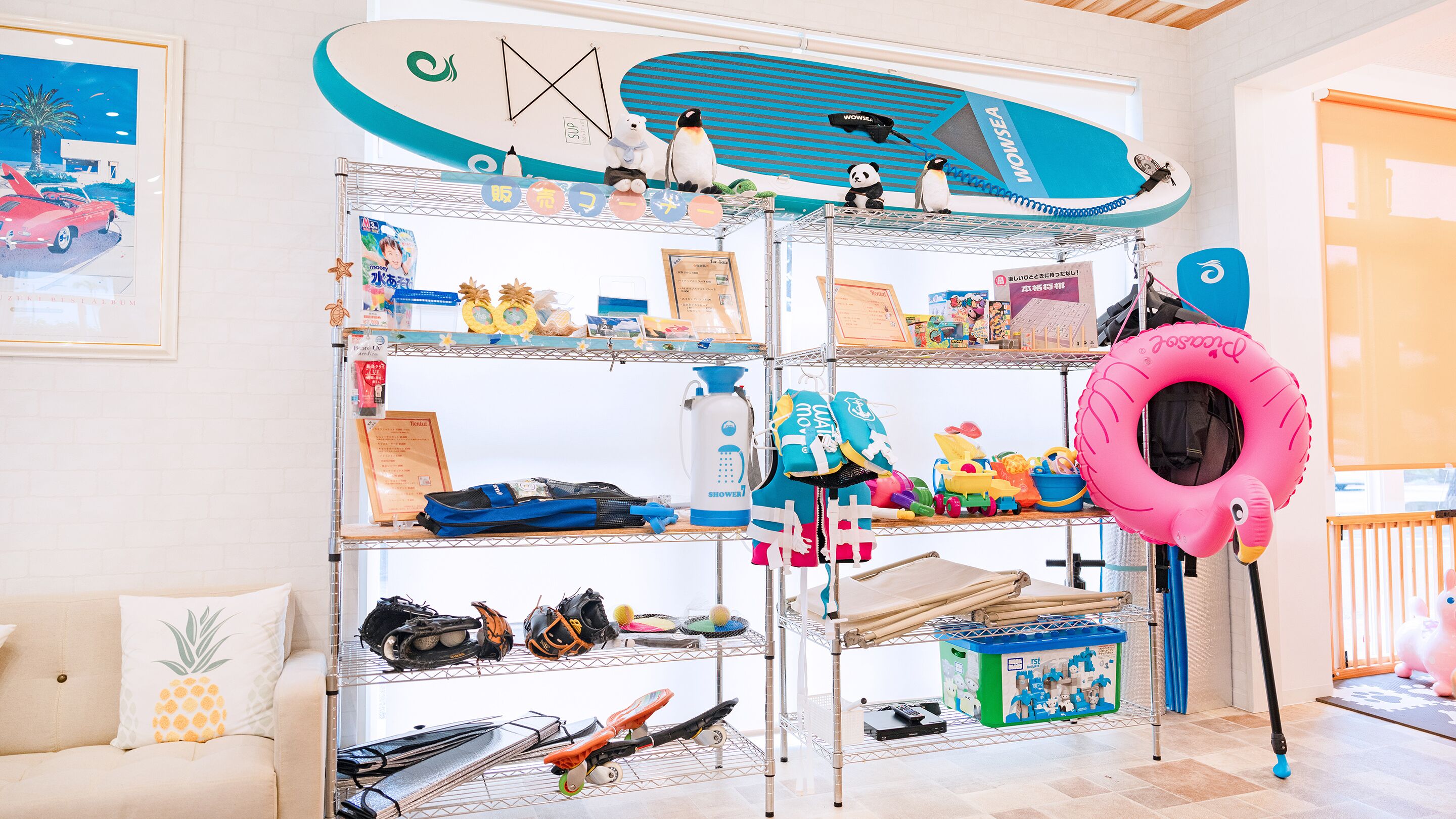 Ein Zimmer mit einem Etagenbett, einer kleinen Couch und einem Regal mit verschiedenen Gegenständen, darunter ein Surfbrett, Spielzeug und ein pinkfarbener Schwimmreifen.