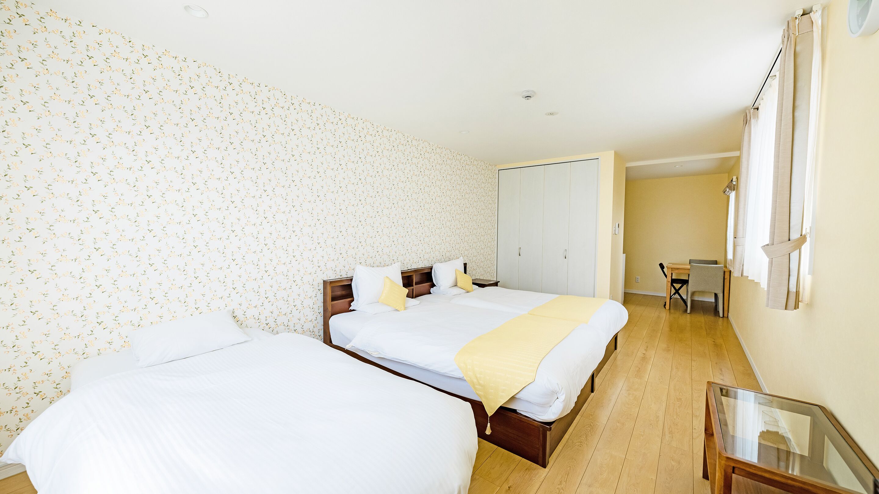 A hotel room with two beds, a wooden floor, a small table, and a wardrobe.