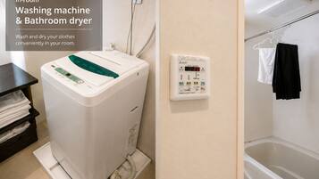 A washing machine and bathroom dryer in a room with a bathtub and a towel rack.