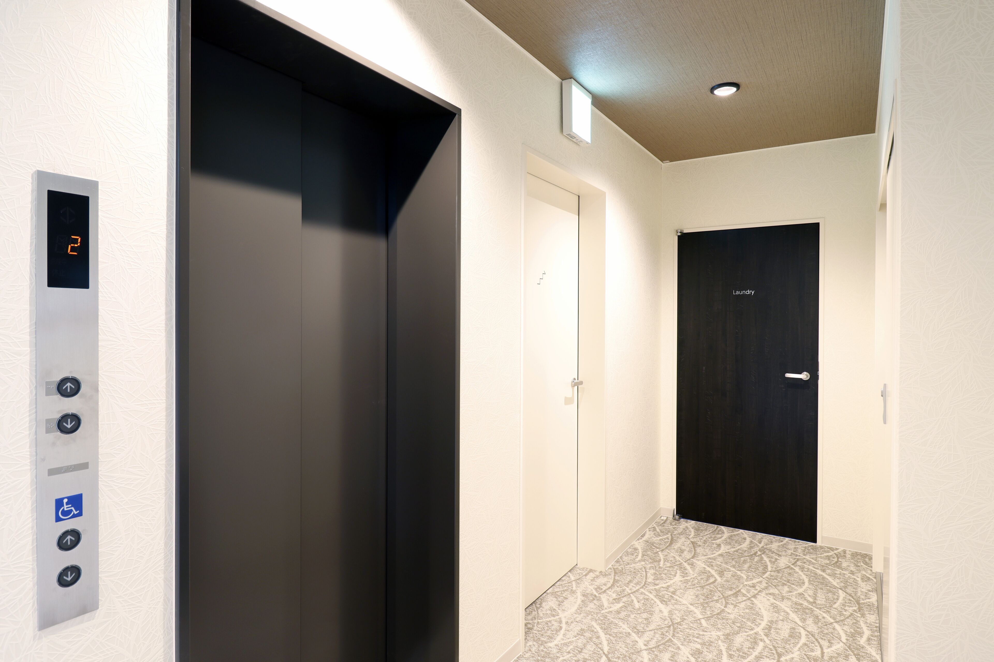 A hallway with an elevator, a door labeled "Laundry," and a wall-mounted elevator control panel.