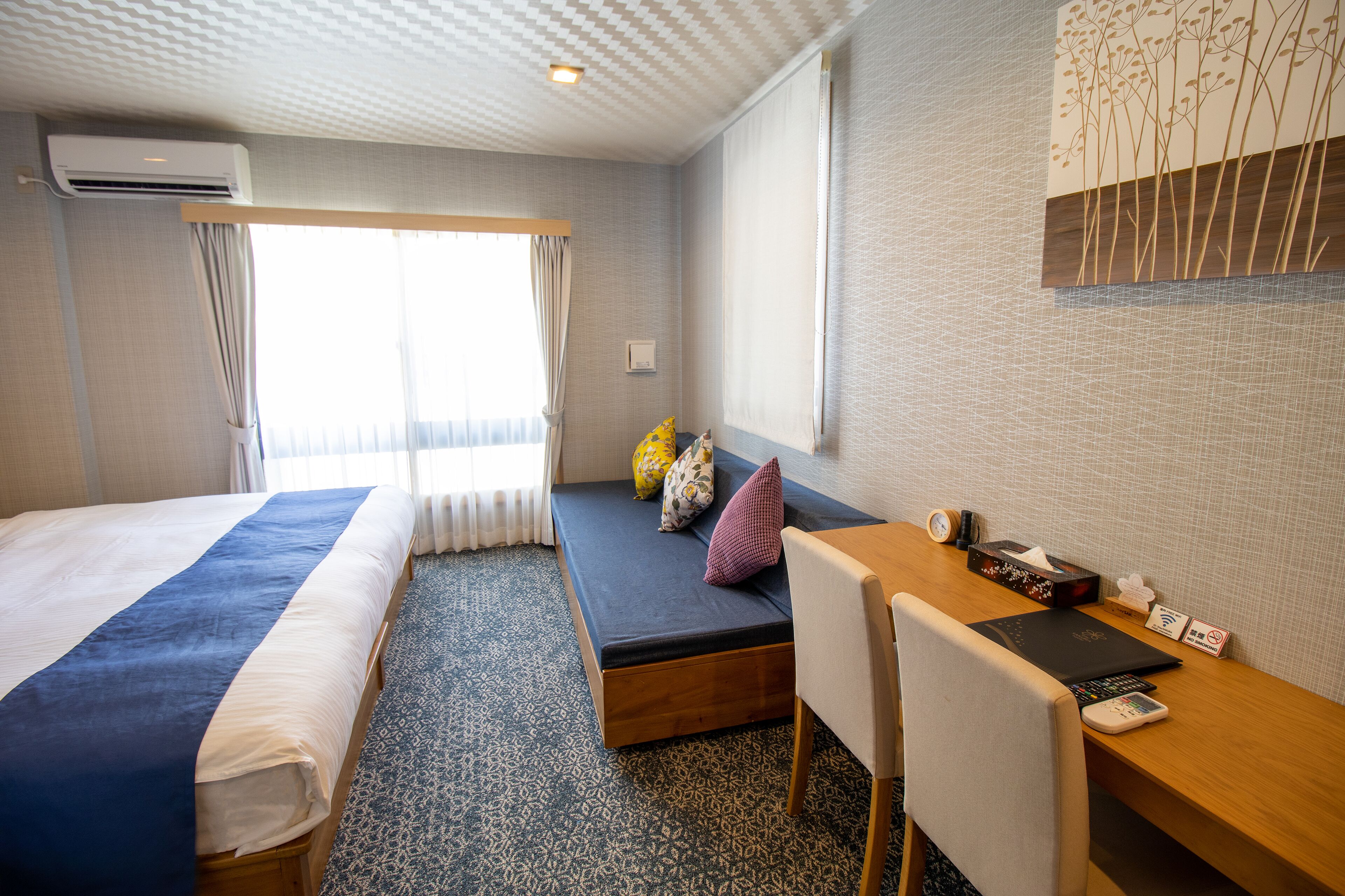 Habitación de hotel con dos camas, un escritorio con una computadora portátil, una silla y una ventana con cortinas.