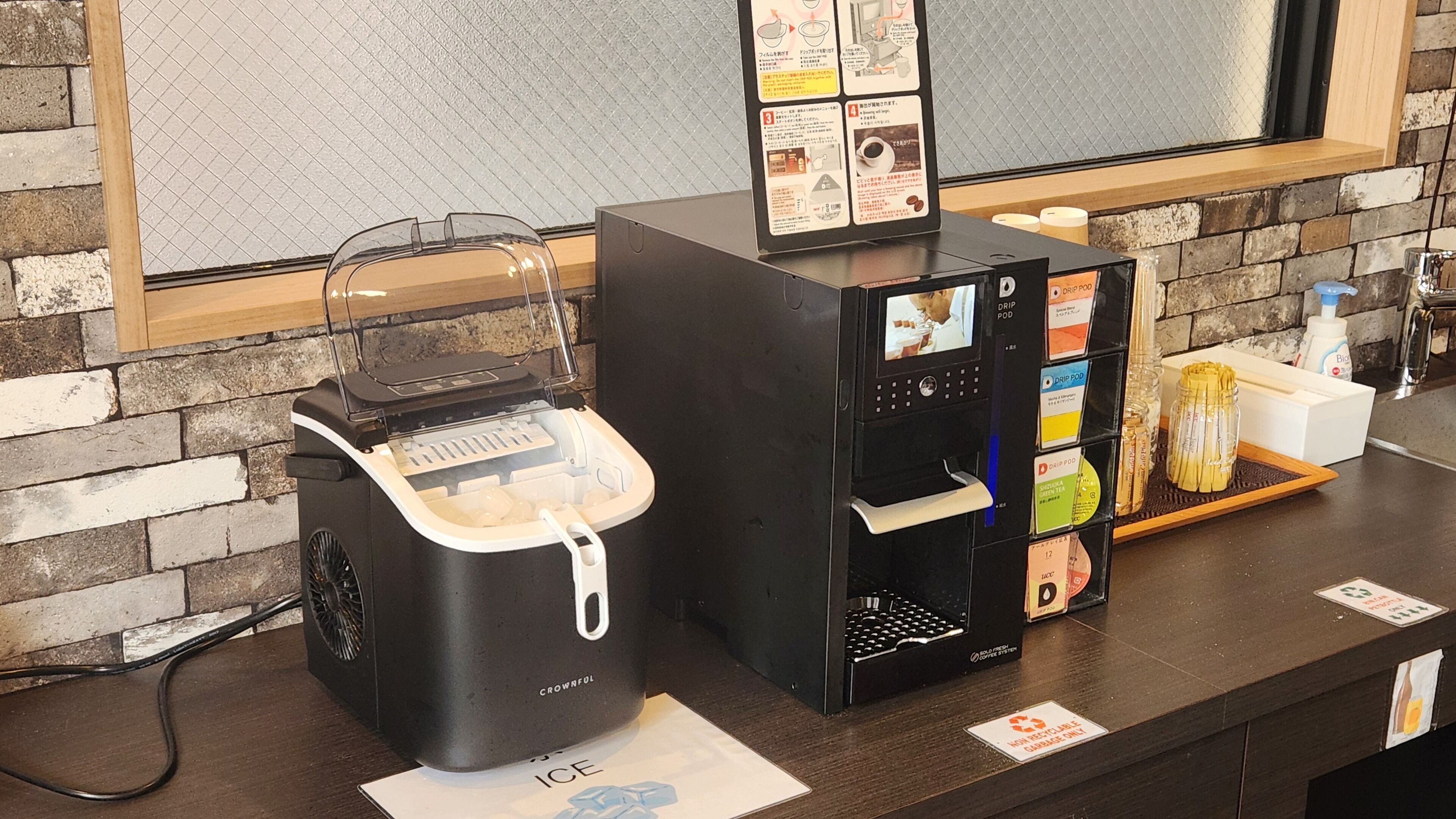 A coffee machine and a drip pod dispenser on a counter with a brick wall background.