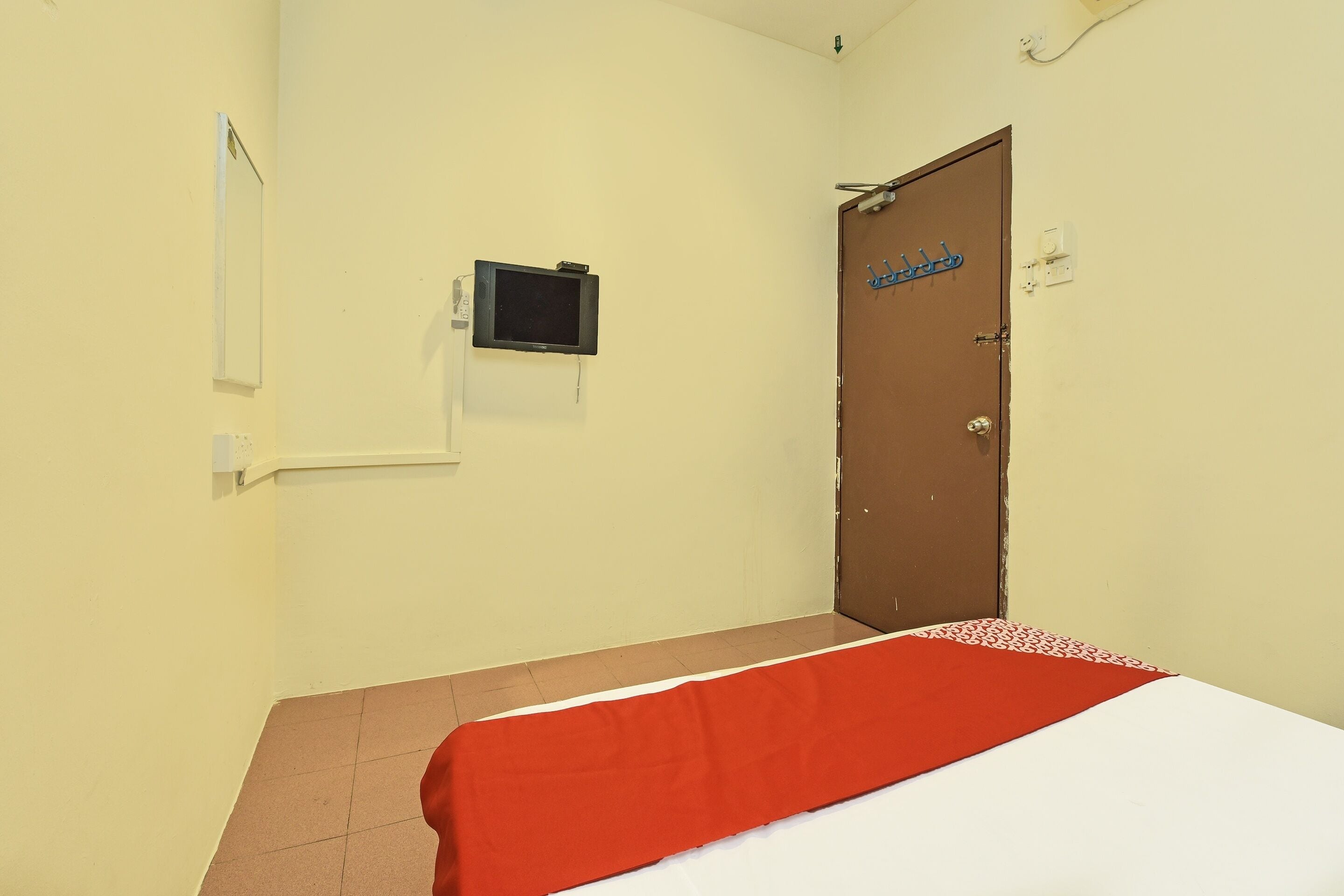 Habitación de hotel con una cama, un televisor montado en la pared y una puerta con un cartel.